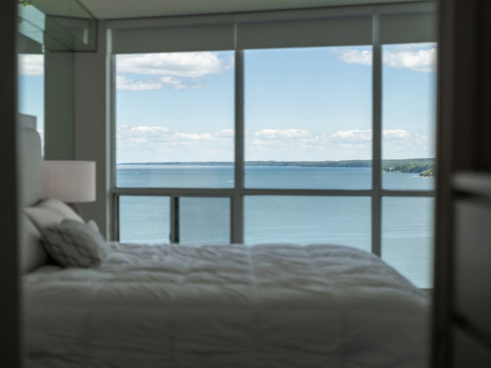 Bed with white linen facing a large window over the sea