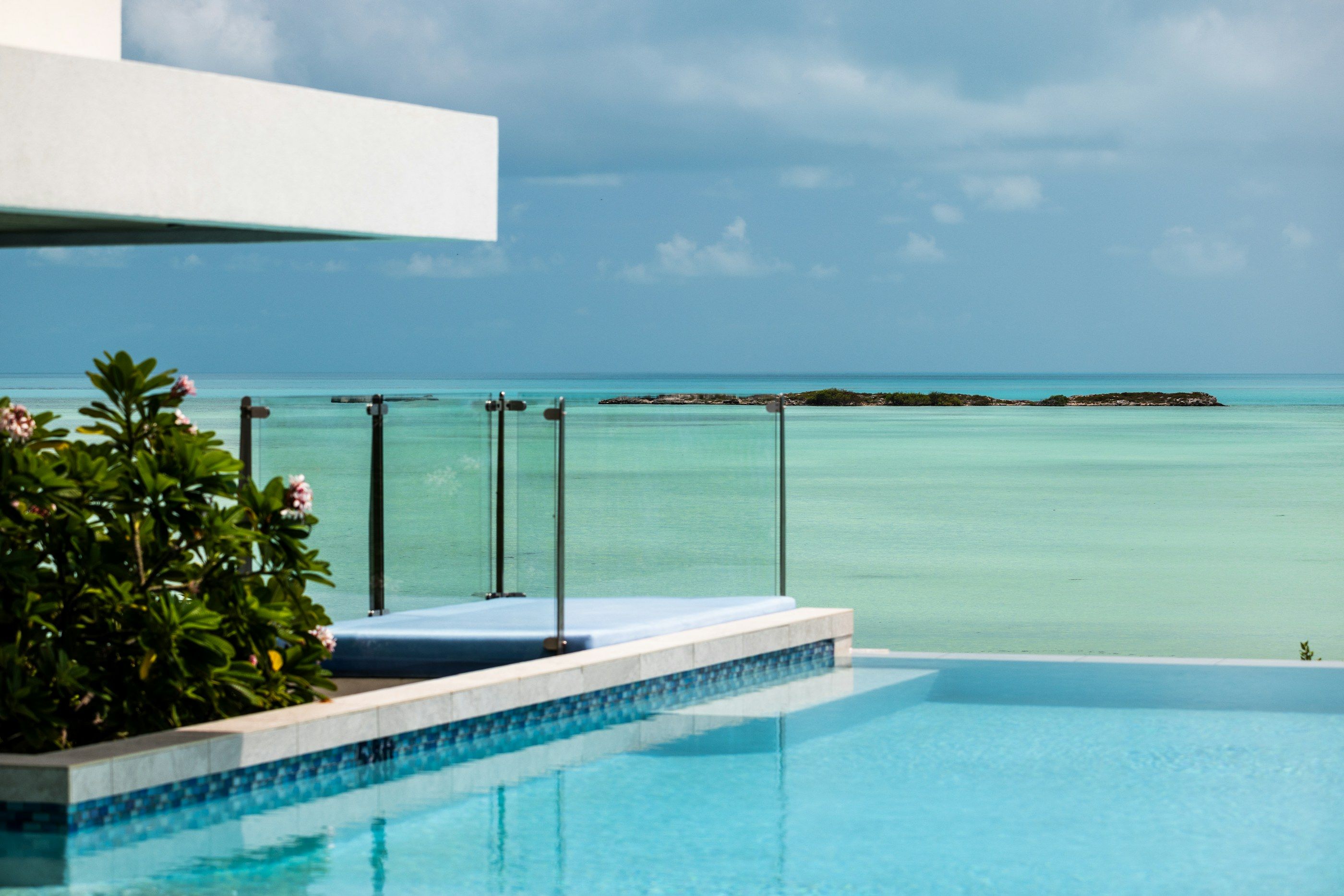 White villa terrace with an infinity pool and glass balustrade overlooking calm turquoise sea and a low island