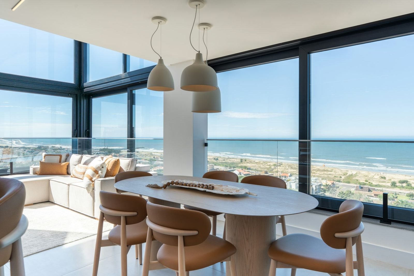 Dining table and lounge behind floor-to-ceiling windows overlooking the sea