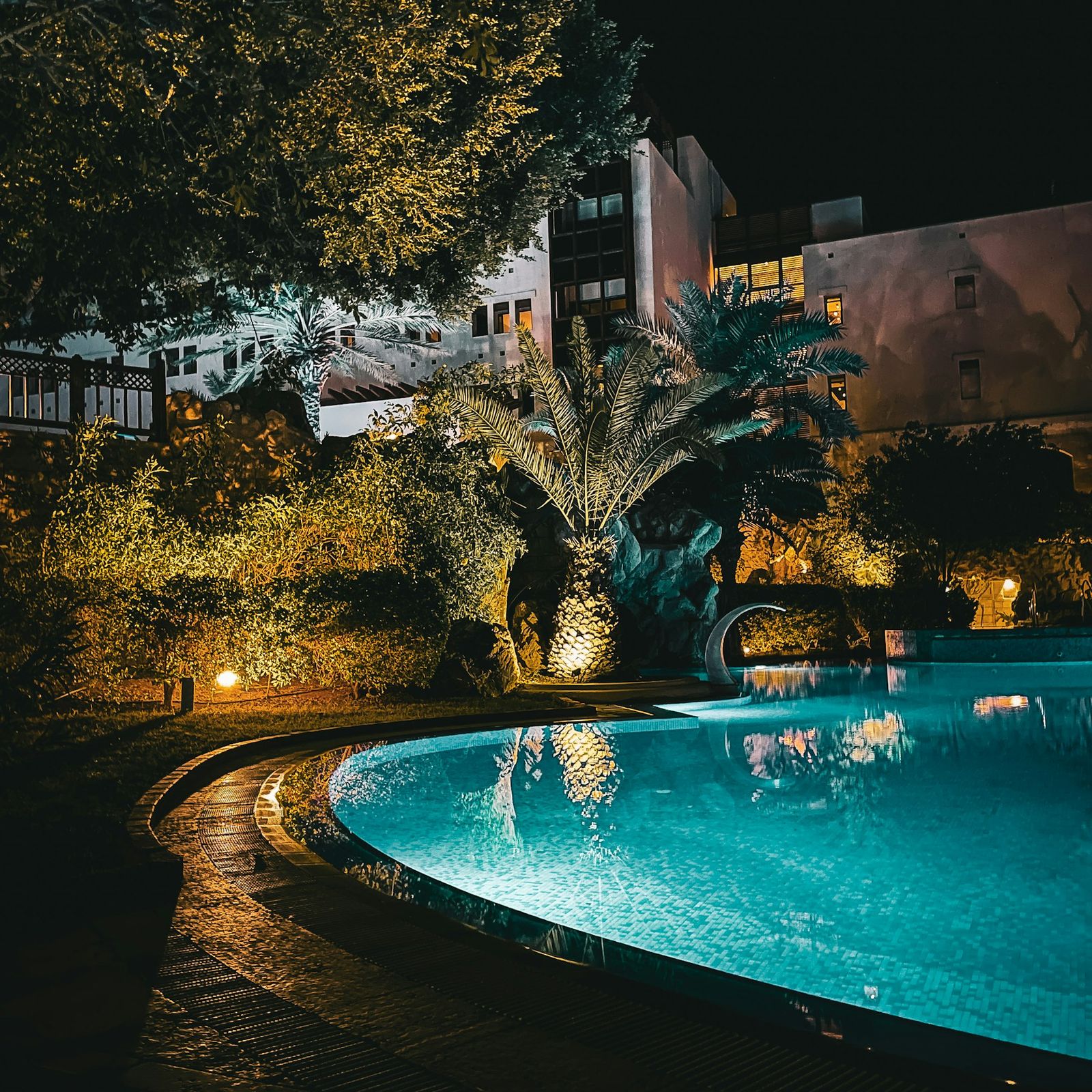Pool and garden lit softly among palms and plants in the evening