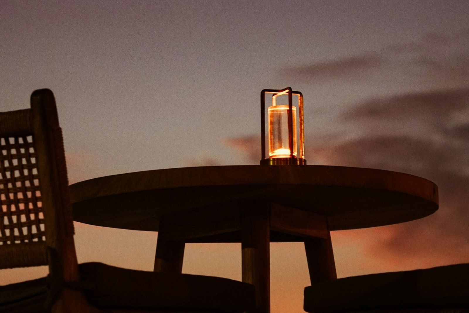 Round table with a lantern on a terrace as the sun sets over the sea