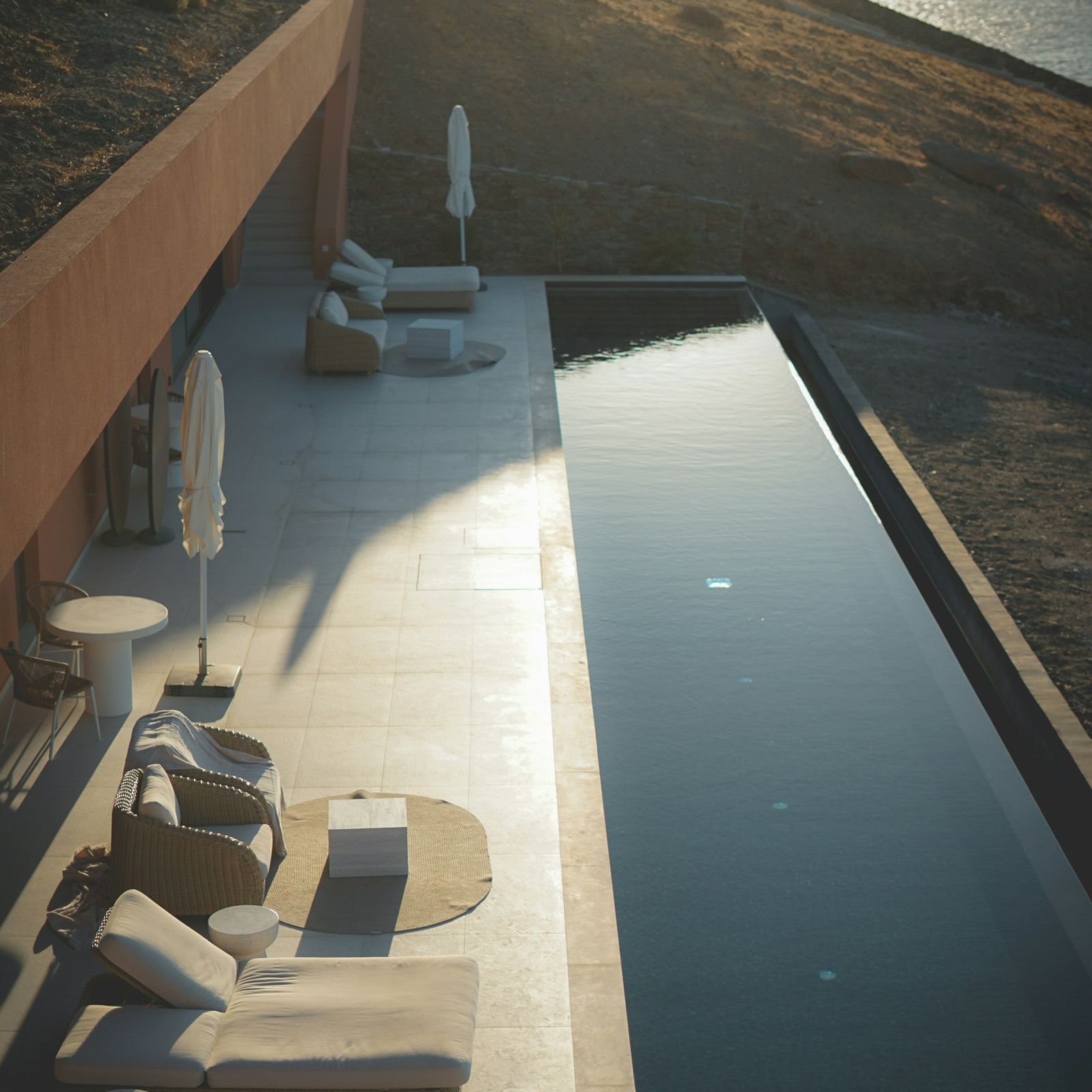 Minimal stone terrace with a narrow infinity pool and loungers at dusk