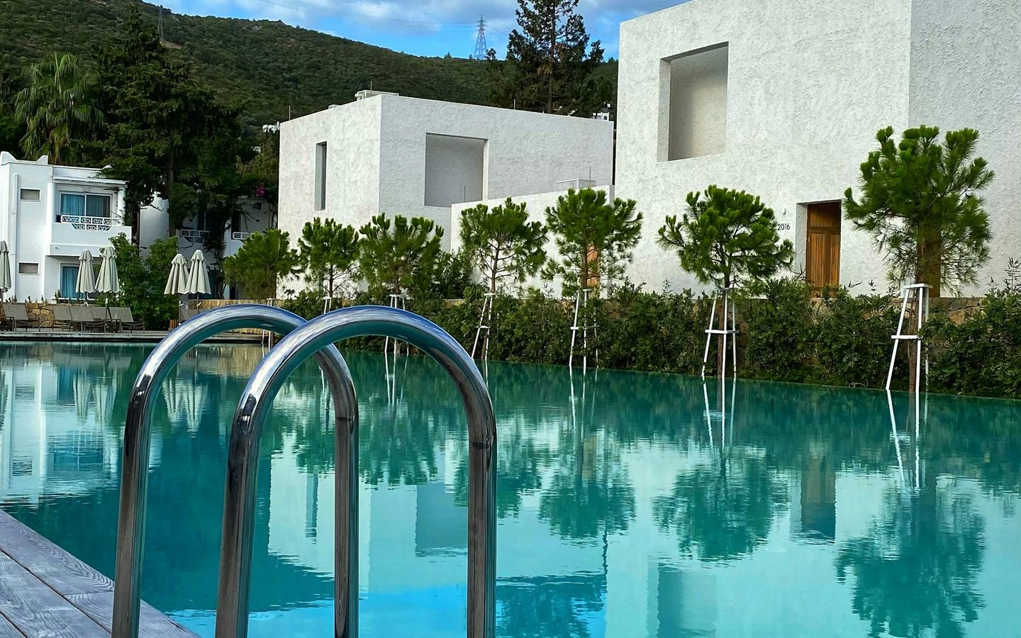 White cubic villa among olive trees reflected in a long private pool