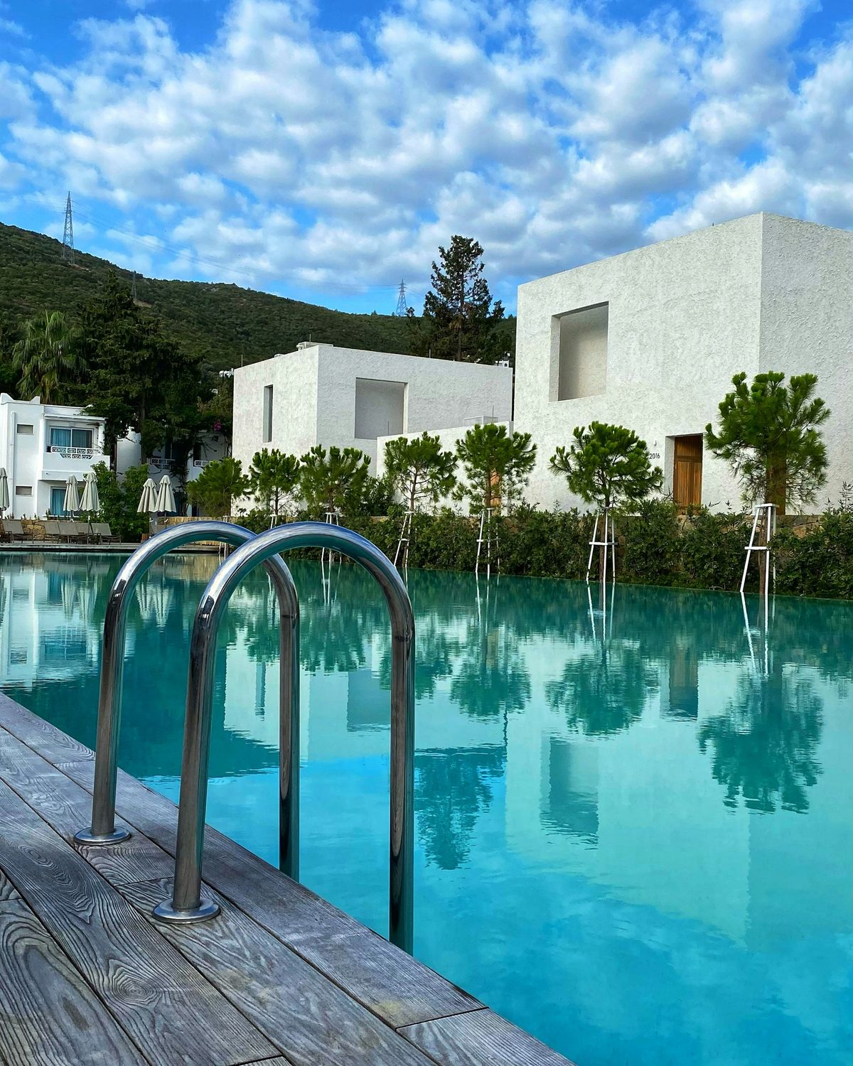 White cubic villa among olive trees reflected in a long private pool